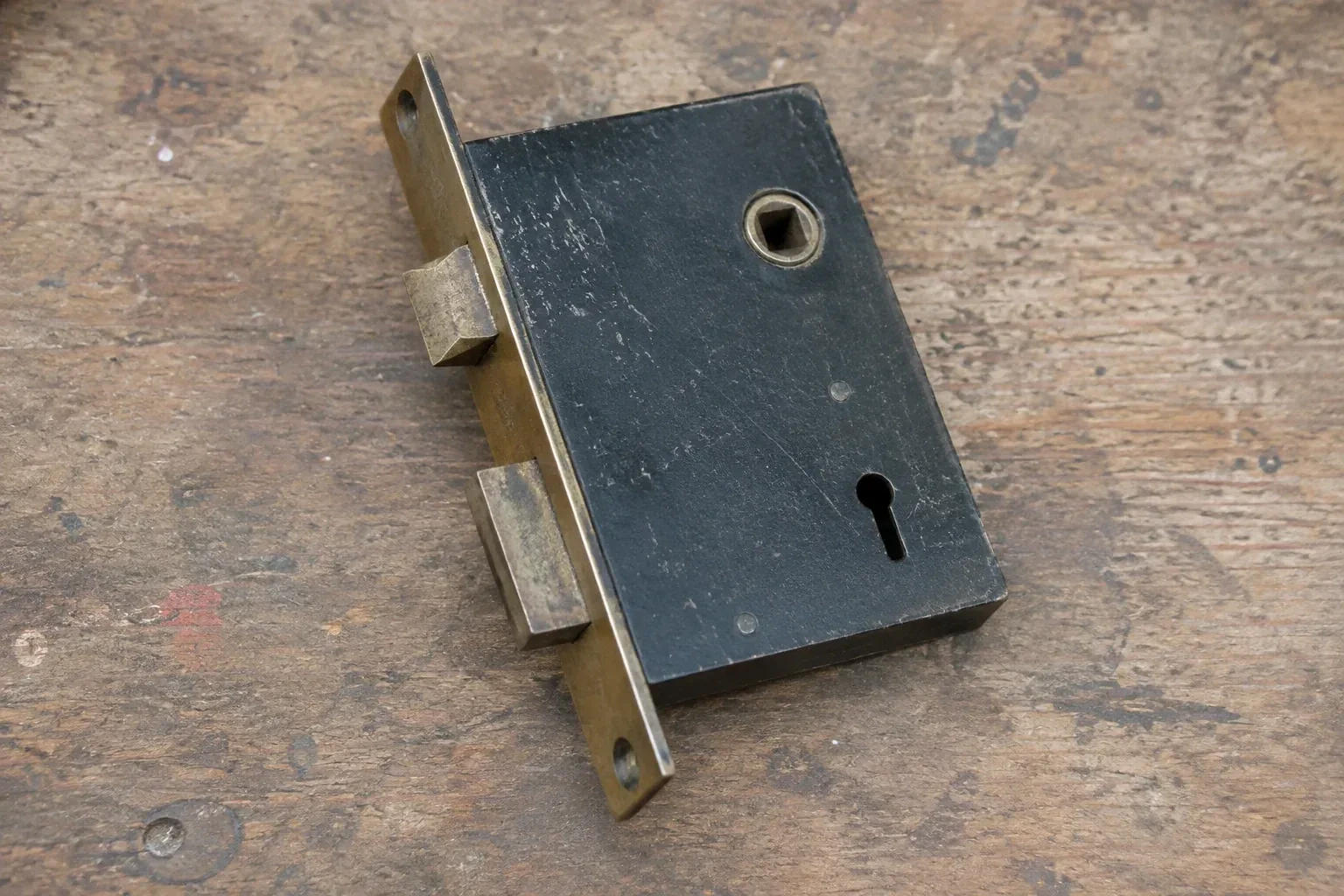 Closed mortise lock case with spindle opening, keyhole, latch and deadbolt on a wooden workbench. — Vintage Mortise Lock Service, Central