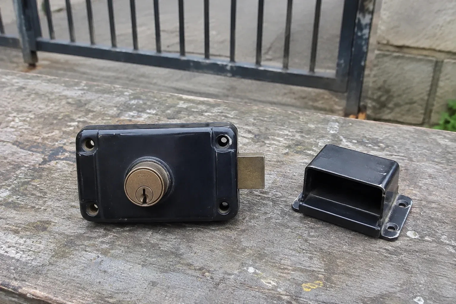 Detached rim gate lock and separate box keeper on an outdoor workbench. — Gate & Building Entry Locks, Hamilton
